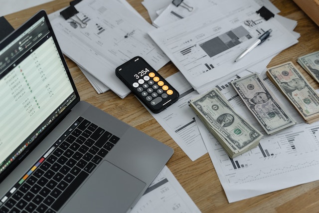 Documents, dollar bills, a calculator and a laptop on a table